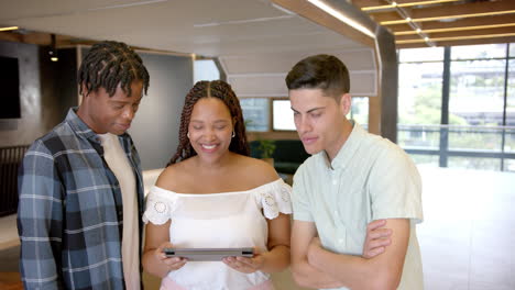 smiling group of young professionals holding tablet, collaborating in modern office