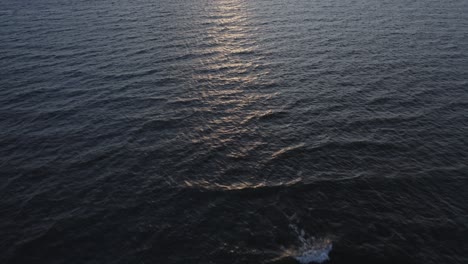 Aerial-of-flight-over-sea-tilting-slowly-towards-sunset