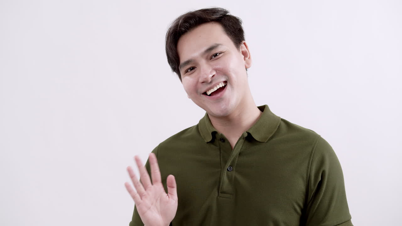 A cheerful man waves hello in a minimalistic studio showcasing warmth and friendliness.