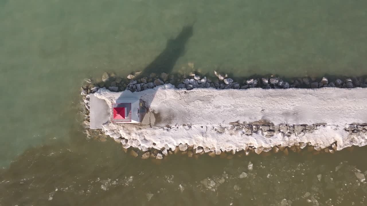 A snow-covered pier with a lighthouse in Southampton, serene waters, aerial view