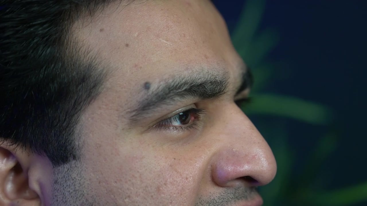 Primo piano macro estremo del volto di profilo di un giovane uomo che guarda altrove durante un'intervista o una sessione di conversazione in uno studio di podcast.