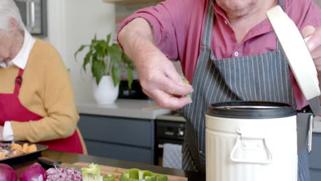 Senior-caucasian-couple-cleaning-vegetable-peels-in-kitchen-at-home,-slow-motion