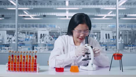 científica asiática mirando a través de un microscopio en la mesa con un tubo de ensayo luego sonriendo y diciendo wow en el laboratorio, trabajando en el laboratorio analizando muestras bajo el microscopio