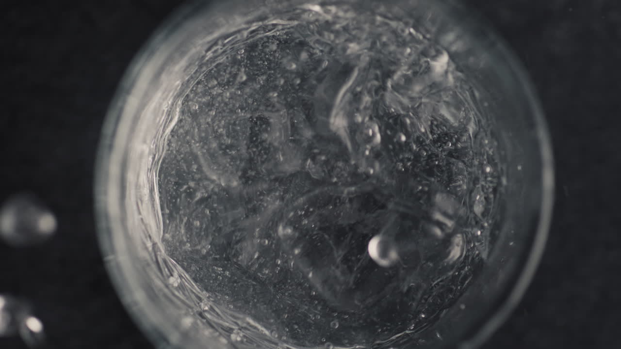 Primo piano di mani che lanciano un cubetto di ghiaccio in un bicchiere d'acqua. Concetto di preparazione di un cocktail.