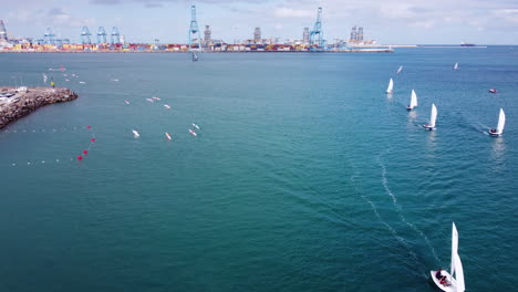 Aerial-shot-over-the-water,-sailing-boats-and-surf-ski-boats,-pier-on-the-left-and-port-on-the-horizon