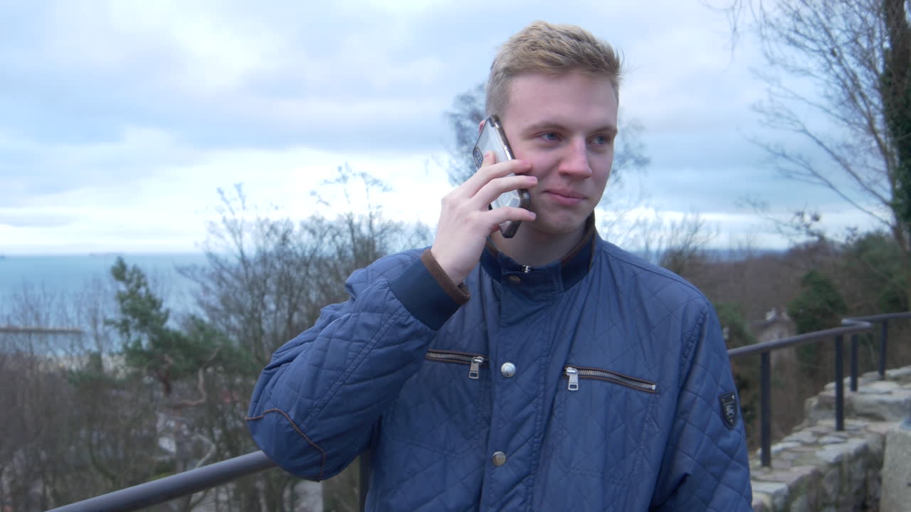 공원에서 스마트폰으로 이야기하는 금발 밀레니엄 세대의 중간 패닝 샷