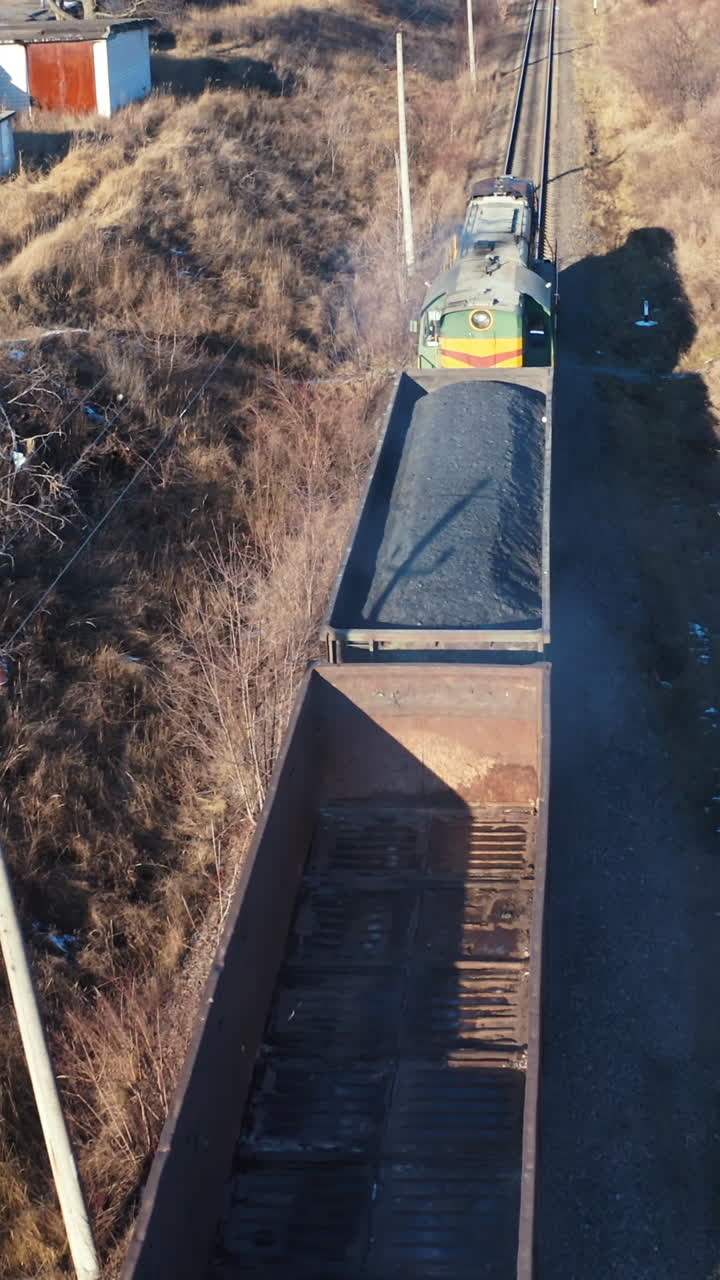 Freight train moving in winter. Top view on a cargo train on rails. Freight transport, railroad and transportation concept. Aerial view. Vertical video