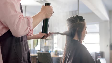 Peluquero-Caucásico-Rociando-El-Cabello-De-Una-Clienta-Feliz-Con-Agua-En-El-Salón,-Cámara-Lenta