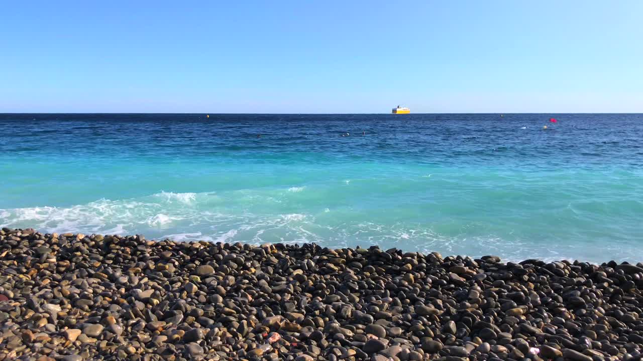 Pebble beach in Nice France, pebble beach stones with turquoise sea water and blue sky, motion of the water