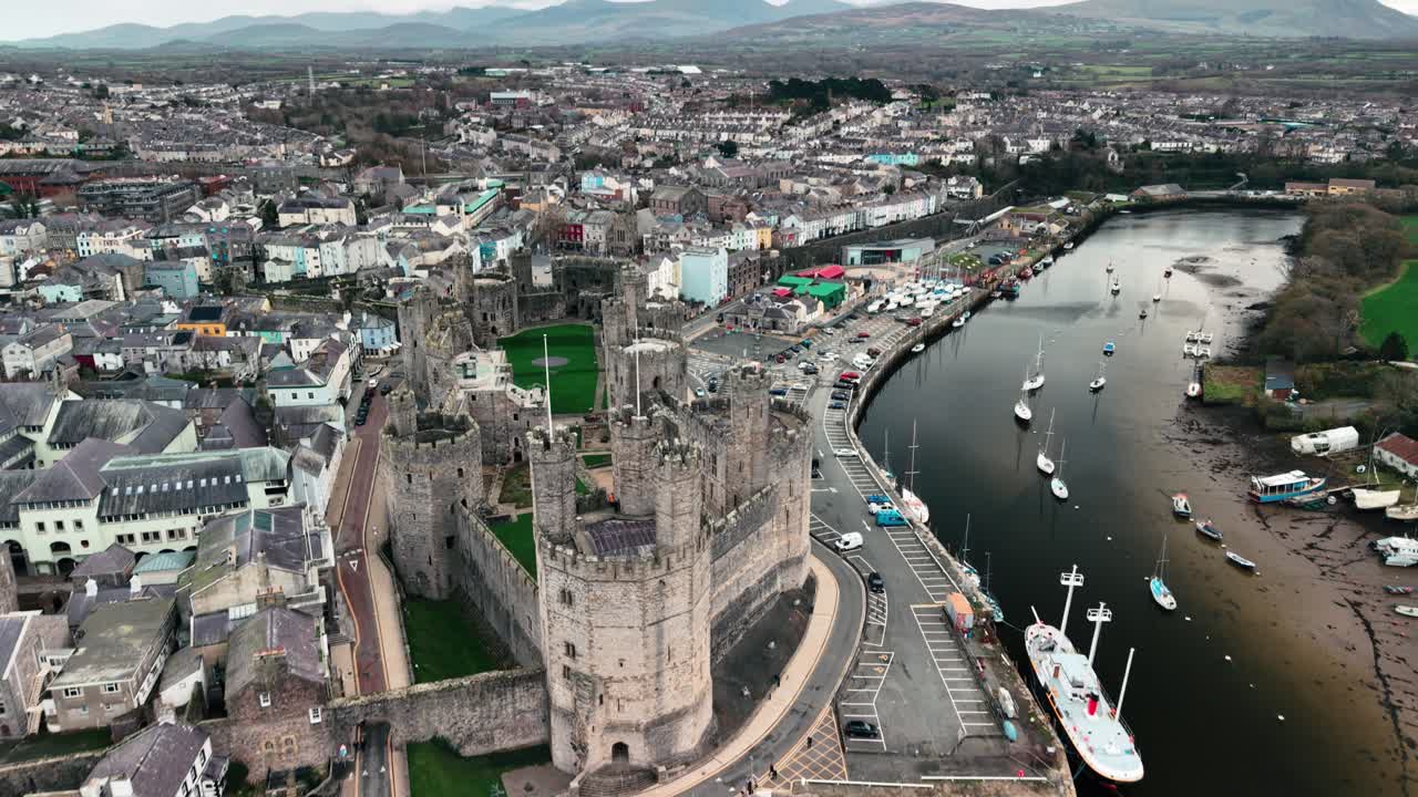 โดรนค่อยๆ หมุนตามเข็มนาฬิกา เผยให้เห็นภาพมุมสูงตระการตาของปราสาท Caernarfon บริเวณปากแม่น้ำ นอร์ทเวลส์ สหราชอาณาจักร