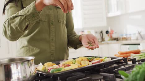 Video-of-midsection-of-biracial-woman-preparing-meal,-adding-herbs