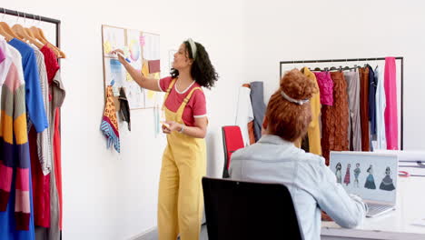 diversas diseñadoras de moda felices usando portátiles y discutiendo diseños en el estudio, en cámara lenta