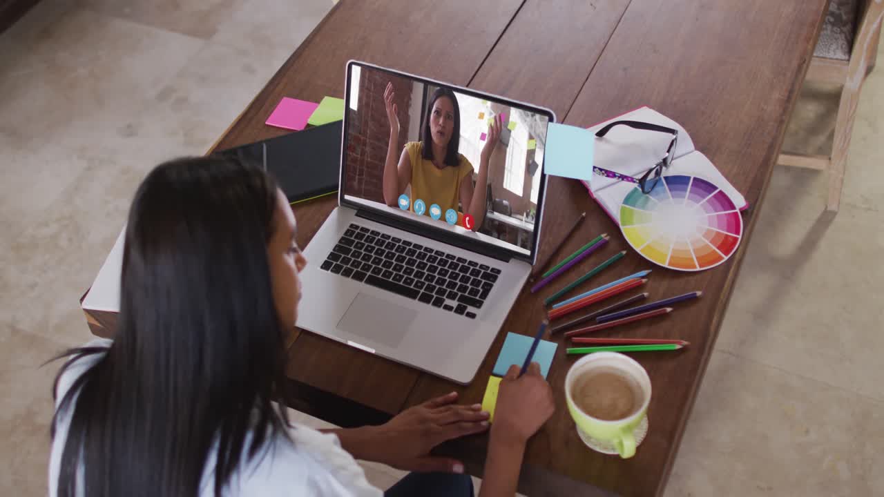 Empresaria mestiza sentada en una mesa usando el portátil haciendo una videollamada con una colega.