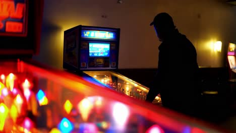 persona jugando a la máquina de pinball en una sala de juegos débilmente iluminada por la noche