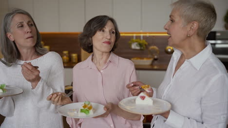 grupo de alegres amigos mayores charlando y comiendo un delicioso postre, parados en una cocina de estilo moderno 2