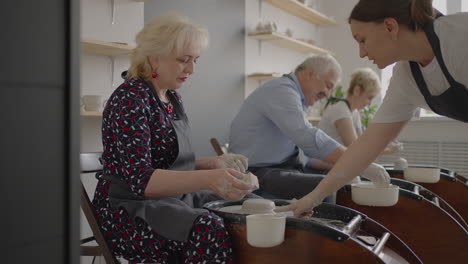 a young woman conducts a pottery class for a group of senior women friends and a man of 60-70 years old. activities for the elderly