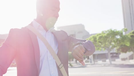 African-american-man-in-city-with-bike-in-the-sun-using-smartwatch