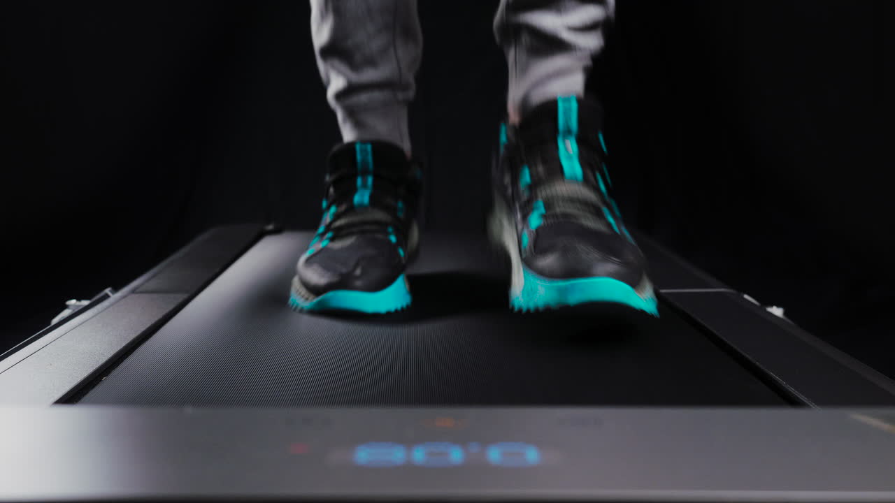 Static frontal close up shot of a man's feet running on a treadmill
