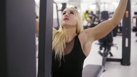 attractive young blond caucasian woman with sporty body training hard on a lat pull-down mashine at the gym. healthy lifestyle concept. rotation footage