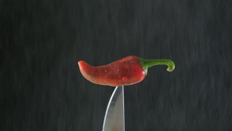 Rote-Chilischote-Steckt-In-Einem-Messer,-Wasser-Rieselt-Auf-Schwarzem-Hintergrund