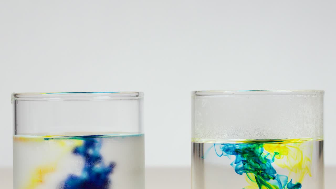 Pipettes drop food coloring into clear water glasses, illustrating diffusion in controlled studio lighting