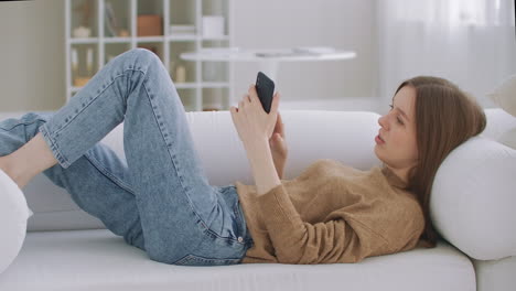 Mujer-En-Una-Videollamada-Usando-Un-Teléfono-Móvil.-Mujer-Madura-Hablando-Por-Teléfono-Inteligente-Mientras-Está-Sentada-En-Una-Sala-De-Estar-Con-Un-Interior-Moderno.-Concepto-De-Tecnología-Y-Relajación.