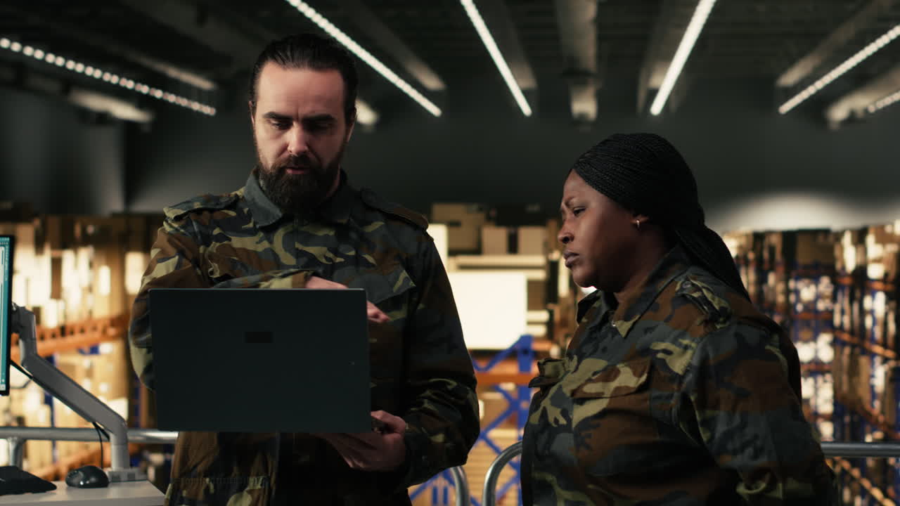 Squadra di logistica militare che discute dell'inventario in magazzino con un laptop.