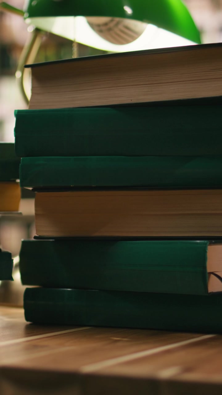Vertical Video Stacked green hardcover books on desk in empty academic library
