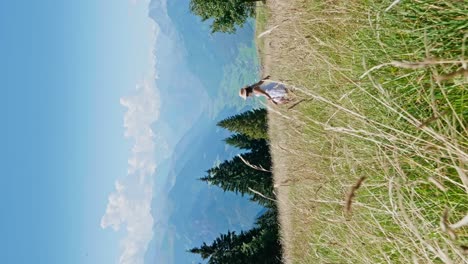 toma vertical de una mujer feliz con falda blanca saltando en un campo de hierba verde durante un día soleado - hermosa cordillera y valle en el fondo - cámara lenta
