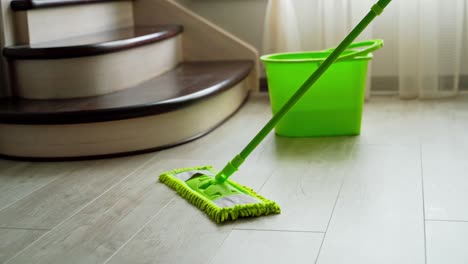 cleaning the floor in the living-room. microfiber mop dusting the parquet floor near the green bucket in the room. householding chores.