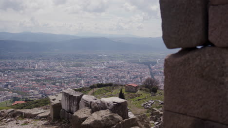 una pared de piedra en primer plano con una ciudad y montañas en el fondo en pérgamo