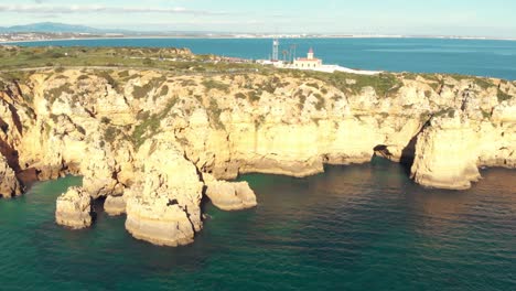 Ponta-da-Piedade-limestone-coastline-and-lighthouse-over-clifftop,-Lagos,-Algarve---Aerial-wide-panoramic-shot