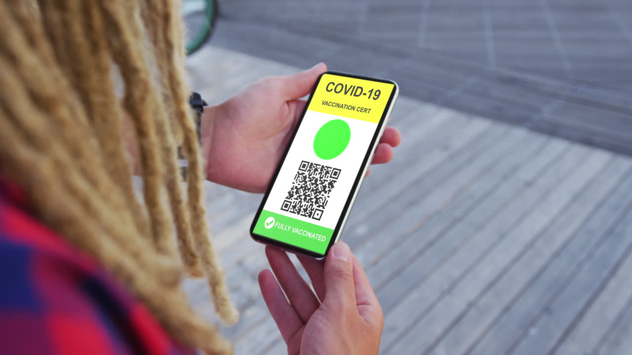 Man with dreadlocks holding smartphone with covid vaccination certificate and qr code on screen