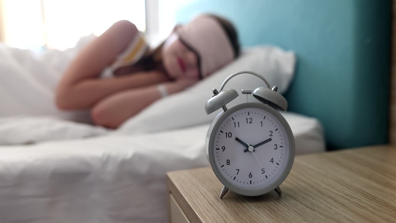 アイマスクを着けてベッドで眠る女性またはティーンエイジャー、そして午前10時の目覚まし時計。