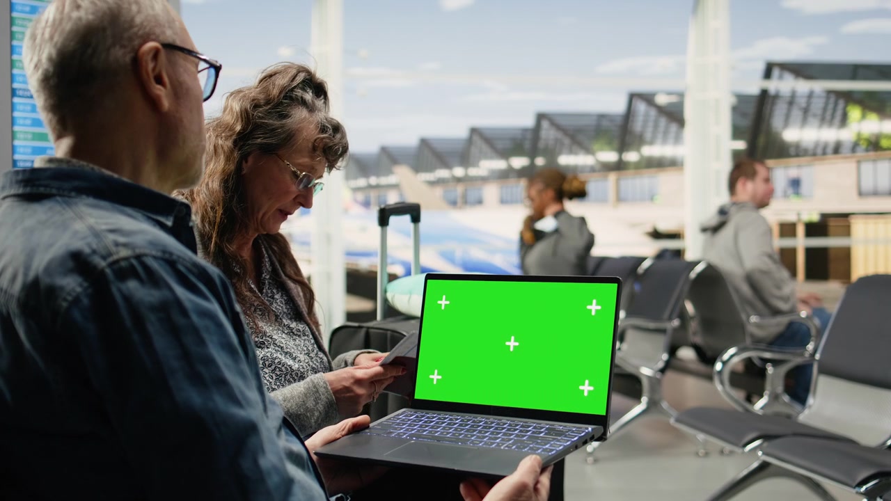 Laptop con schermo verde tenuto da una coppia anziana nella lounge del terminal dell'aeroporto