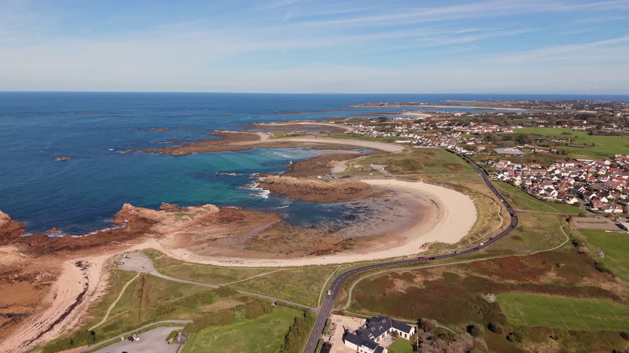 Guernsey Grandes Rocques Channel Islands high drone flight over perfect horseshoe sandy bays with crystal clear water and expansive views over the island on sunny day