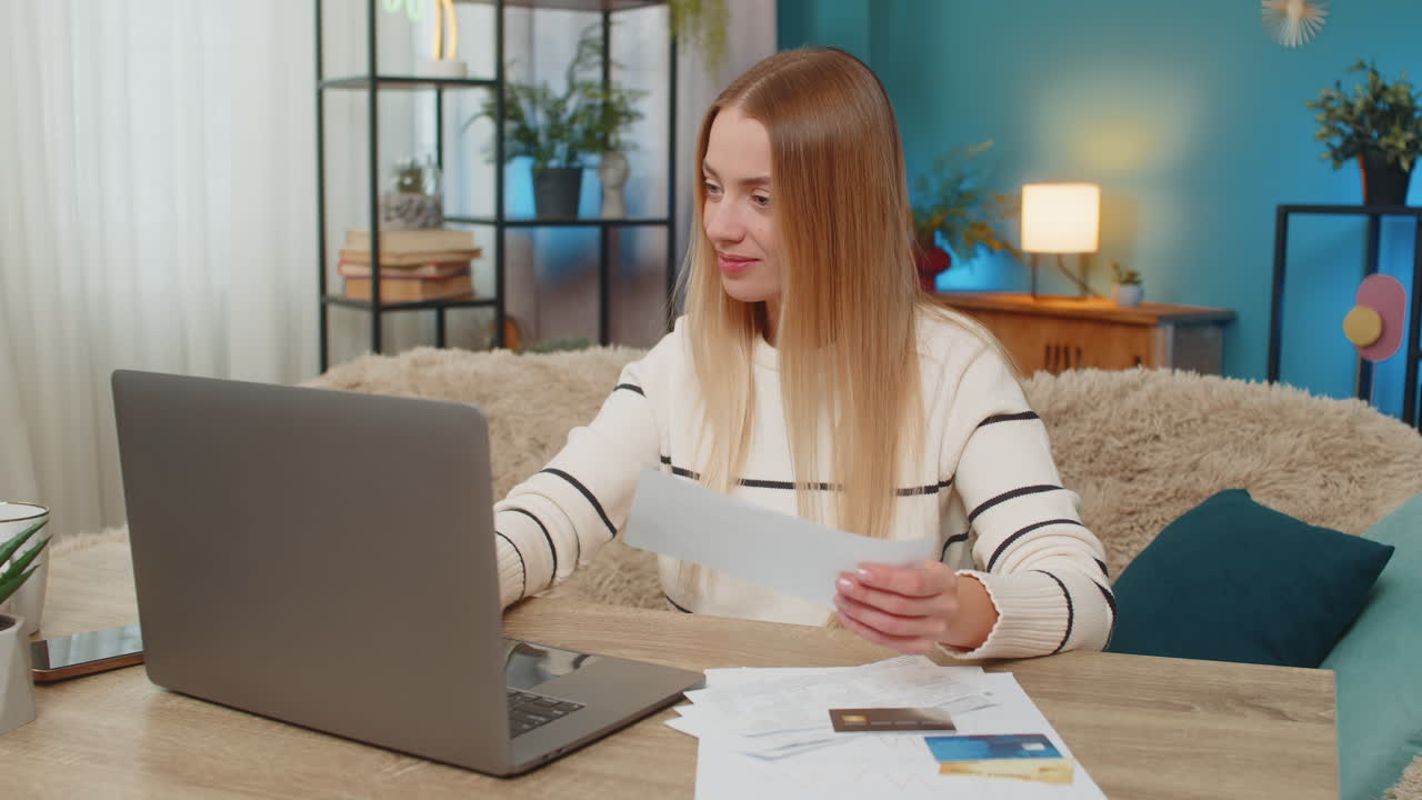 Caucasian woman checking bank account on laptop at home on table with credit cards documents happy