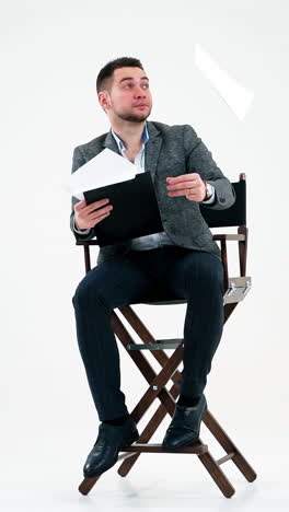 elegant man with a folder. businessman sitting on the chair and reading documents. many papers are flying in the studio over the handsome man. vertical video