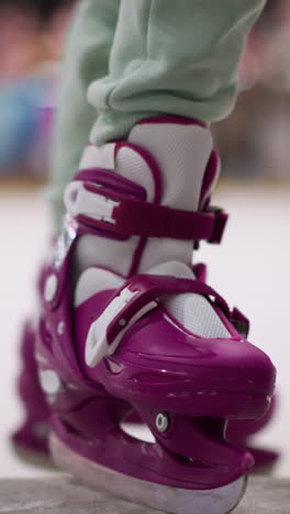 primer plano de una persona con patines de hielo púrpura saliendo de la pista de hielo, el enfoque está en los patines y la parte inferior de las piernas, enfatizando la acción y el movimiento
