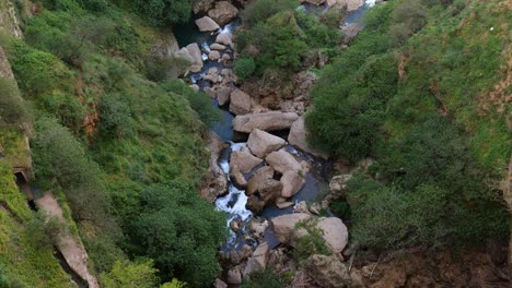 Vista-Aérea-Mirando-Hacia-El-Barranco-Con-El-Río-Corriendo-A-Través-De-Grandes-Rocas-En-Ronda