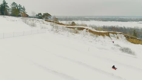 family-downhills-on-red-sledding-tube-down-snowy-white-slope