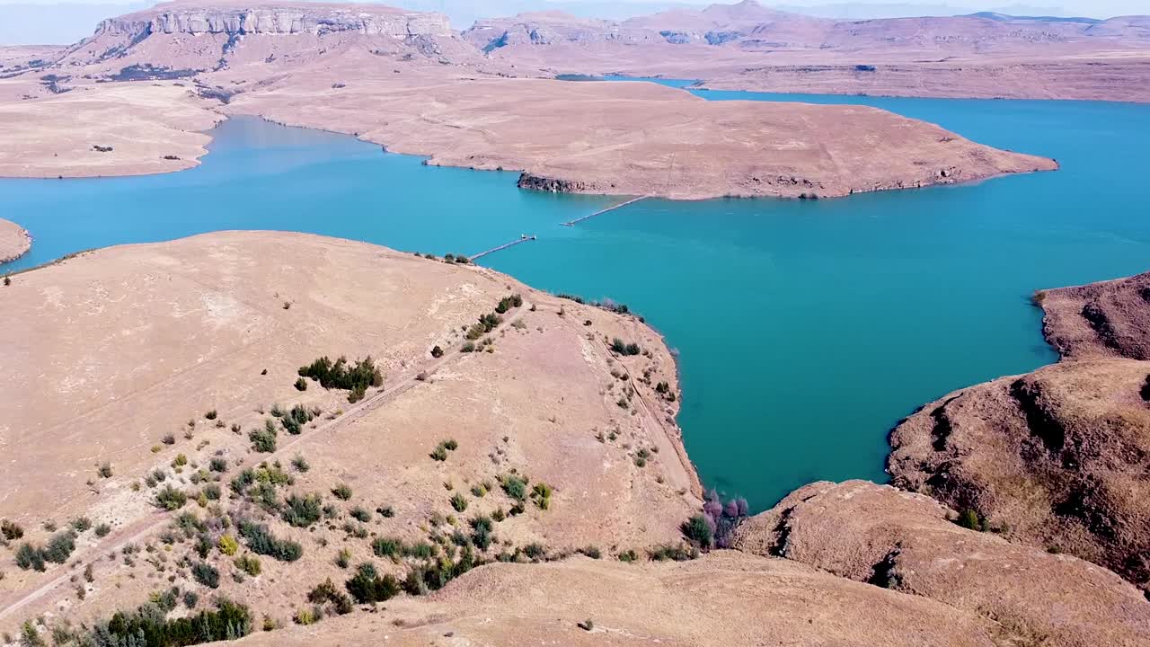toma aérea que viaja sobre el paisaje montañoso seco que rodea la presa driekloof, el embalse es pequeño pero forma parte de la presa sterkfontein más grande en el estado libre, sudáfrica