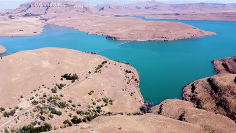 Aerial-shot-travelling-over-the-dry-hilly-landscape-which-surrounds-the-Driekloof-Dam,-the-reservoir-is-small-but-forms-part-of-the-larger-Sterkfontein-Dam-in-the-Free-State,-South-Africa