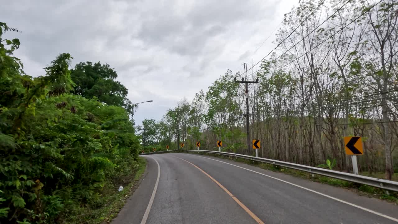 Vehicle travels on winding asphalt road through lush tropical landscape under overcast sky, steady camera