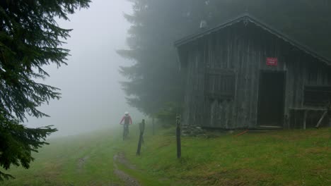 Mountain-biker-rides-past-an-abandoned-house-in-a-foggy-field