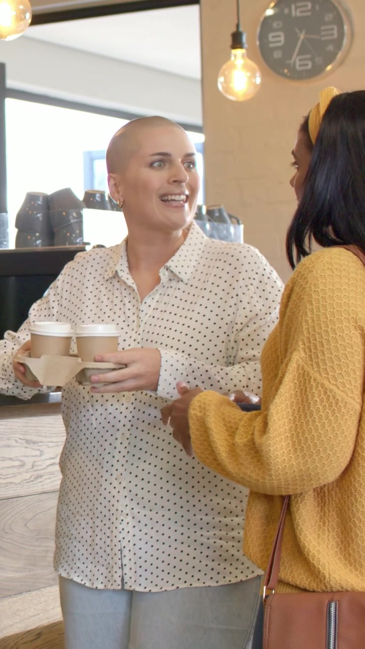 Video verticale: Ospite con maglione giallo che cammina, mentre il personale del caffè offre quattro tazze e usa il telefono.