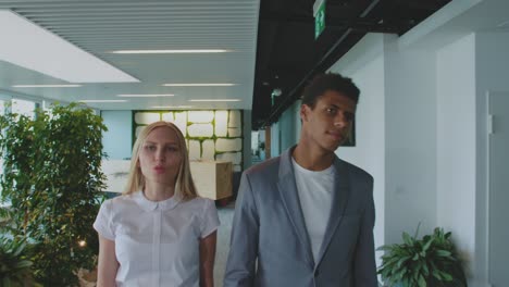 diverse colleagues walking in office and talking. young woman with black man walking in modern office hall and looking around having visit