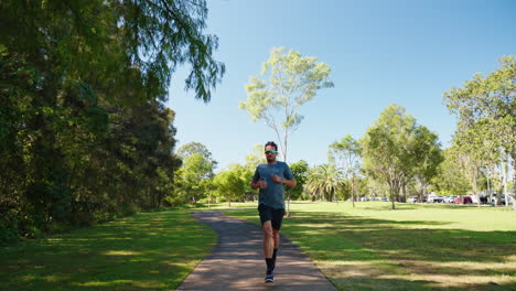 Front-View-Of-Athlete-Man-Running-On-Footpath-In-Park,-4K-Slow-Motion