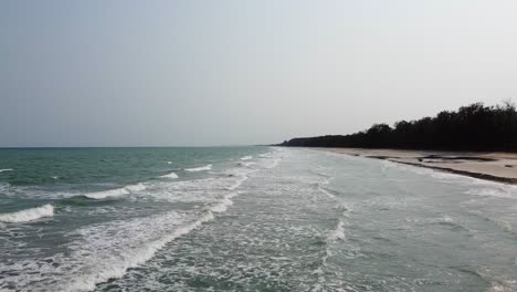 aerial: side view of long ocean waves reach the shore in southern thailand