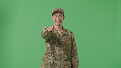 asian man soldier smiling and touching his chest then pointing at you while standing in the green screen background studio